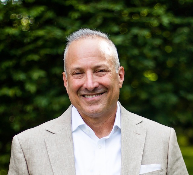 Man in tan suit with white shirt smiling